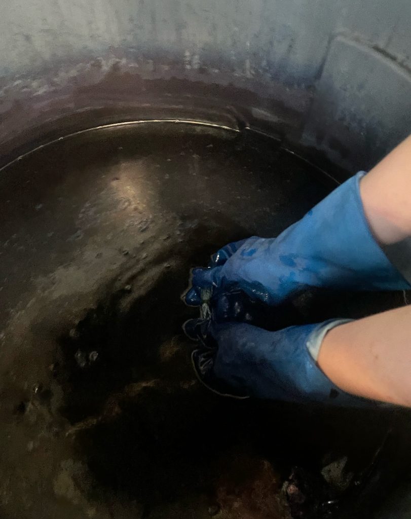 My process Dyeing a warp in an indigo dye vat wearing rubber gloves.