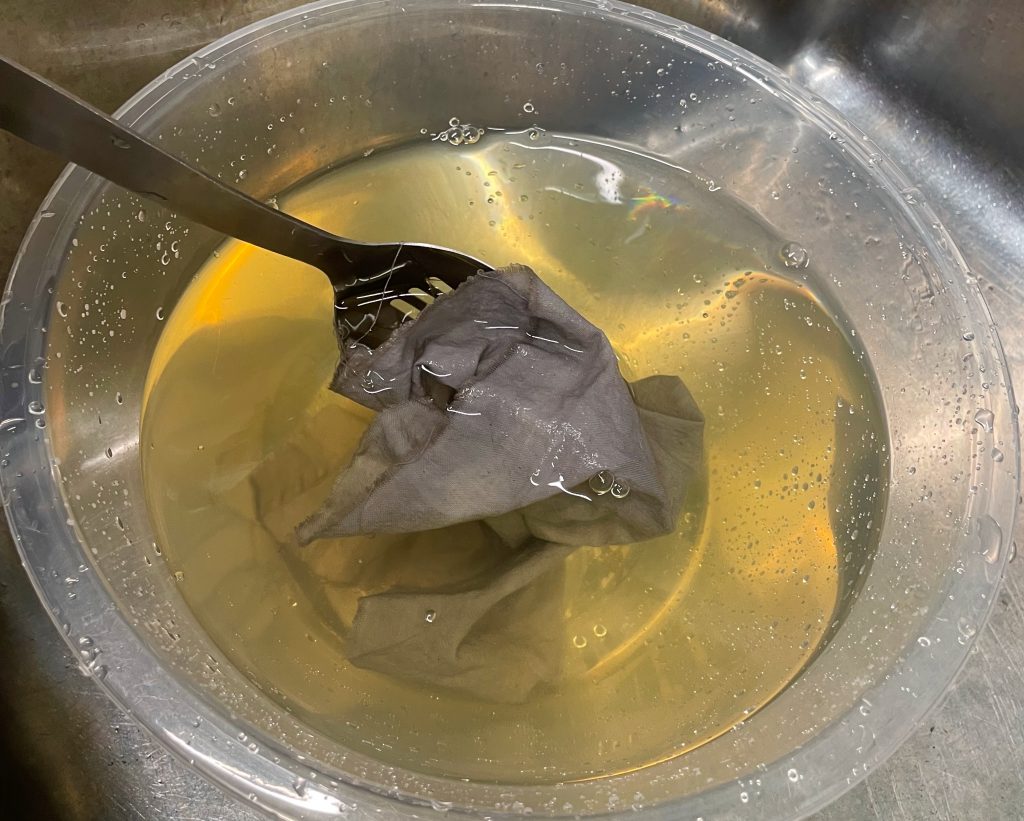 My process A plastic bowl with fabric in submerged in dye, and a metal spoon.